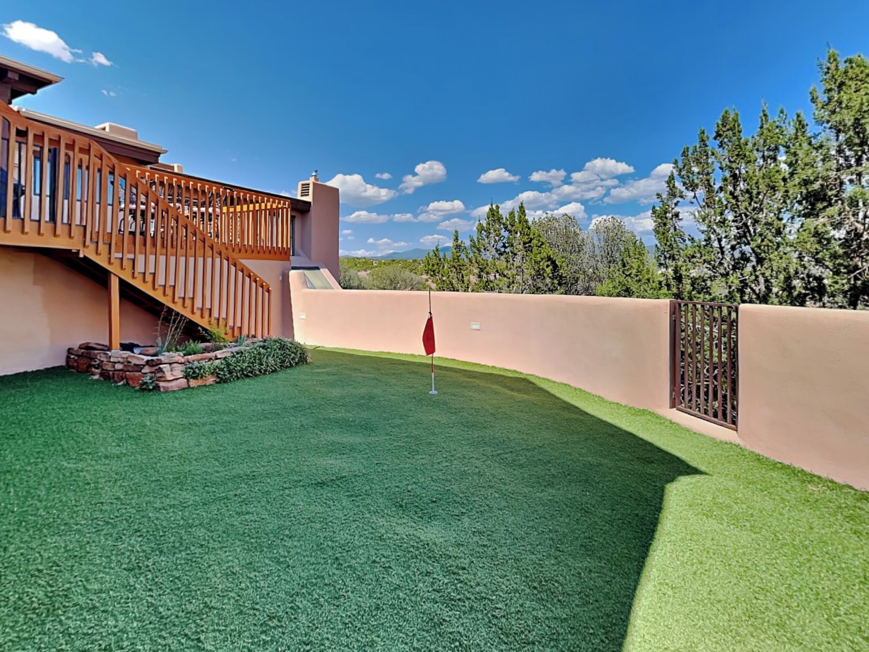 A backyard with artificial grass, a wooden deck, and a stone wall.