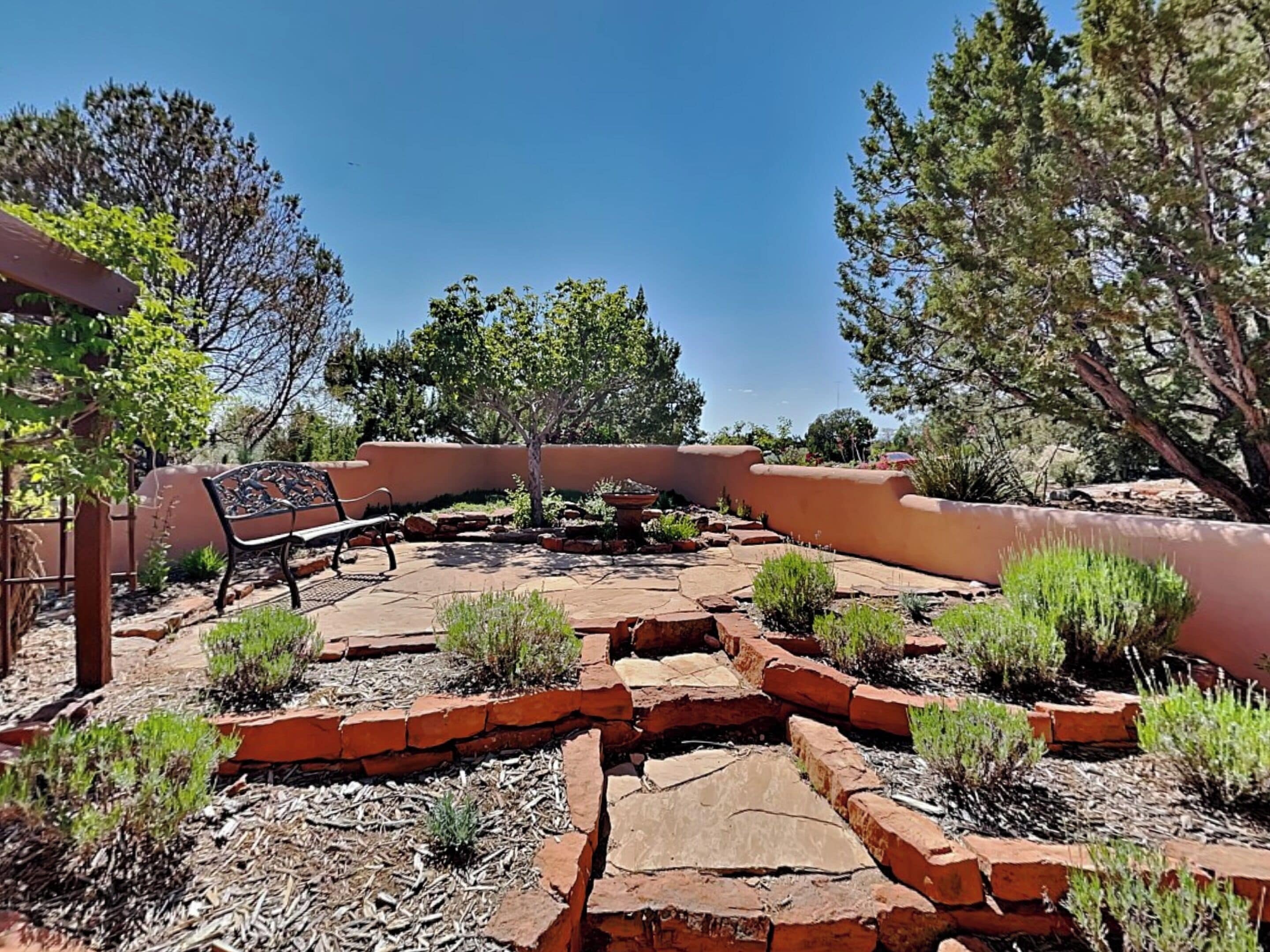 A patio area with a curved bench, surrounded by red brick planters and green shrubs.