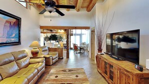 Un salón amplio con un sofá de cuero, un televisor sobre un mueble de madera y un ventilador de techo.