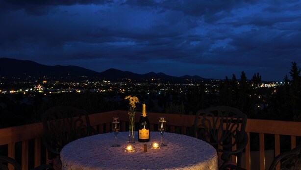 Mesa para dos con una botella y copas, con vistas a un paisaje urbano nocturno.