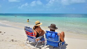 Two people sitting on beach chairs facing the ocean, with clear water and a sandy beach. - Heart designed Apartment, Ocean and Lagoon view, large terrace  (Cancún)