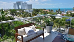 A balcony with a wooden bench, a potted plant, and a dining area with a table set for two. - Heart designed Apartment, Ocean and Lagoon view, large terrace  (Cancún)