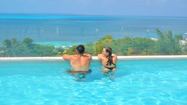 A couple relaxing in a pool with a view of the ocean and tropical landscape. - Heart designed Apartment, Ocean and Lagoon view, large terrace  (Cancún)