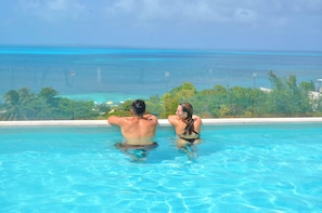 A couple relaxing in a pool with a view of the ocean and greenery. - Heart designed Apartment, Ocean and Lagoon view, large terrace  (Cancún)