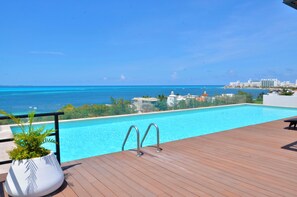 A wooden deck with a pool overlooking a beach and city skyline. - Heart designed Apartment, Ocean and Lagoon view, large terrace  (Cancún)