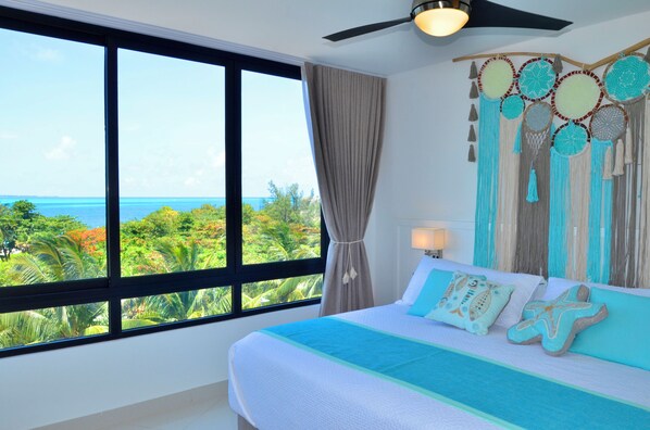 A bedroom with a large window, a bed with starfish pillows, and a wall hanging with circular patterns. - Heart designed Apartment, Ocean and Lagoon view, large terrace  (Cancún)