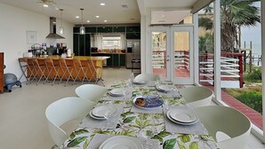 A modern kitchen with a central island, dining area with a table set for six, and a balcony with a view of the sea. - Dock of the Bay by Ryson Vacation Rentals (Galveston)