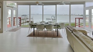 A dining area with a table set for four, large windows offering a view of a body of water and a pier. - Dock of the Bay by Ryson Vacation Rentals (Galveston)