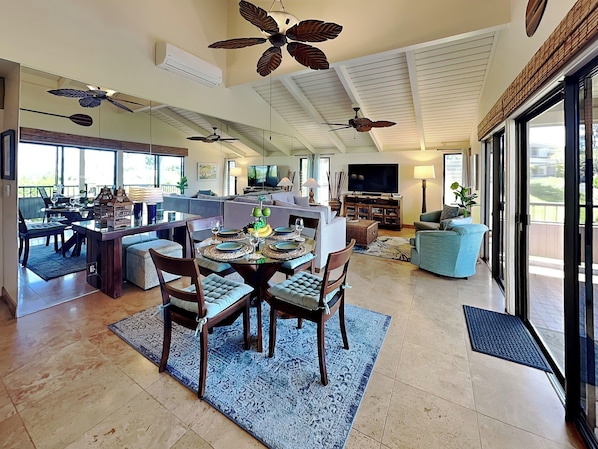 Ein geräumiger Wohnbereich mit Esstisch, Sofas, Fernseher und Deckenventilatoren.