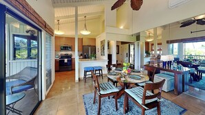 A spacious kitchen with modern appliances, a dining area with a round table and chairs, and a view through a glass door. - Wailea Ekolu Village 1406 by Maui Rental Group (Kihei)