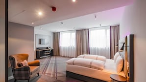 Ett modernt hotellrum med en soffa, fåtölj, TV och ett skrivbord.