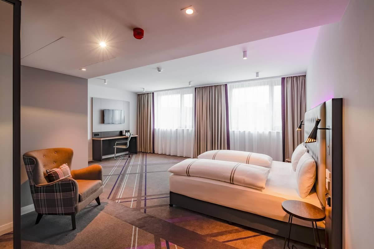 A modern hotel room with a sofa, armchair, TV, and a desk.