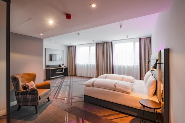 A modern hotel room with a sofa, armchair, TV, and a desk.