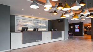 En hotellobby med modern design, med en receptionsdisk, flera hänglampor och en stor vägg med motiverande citat.