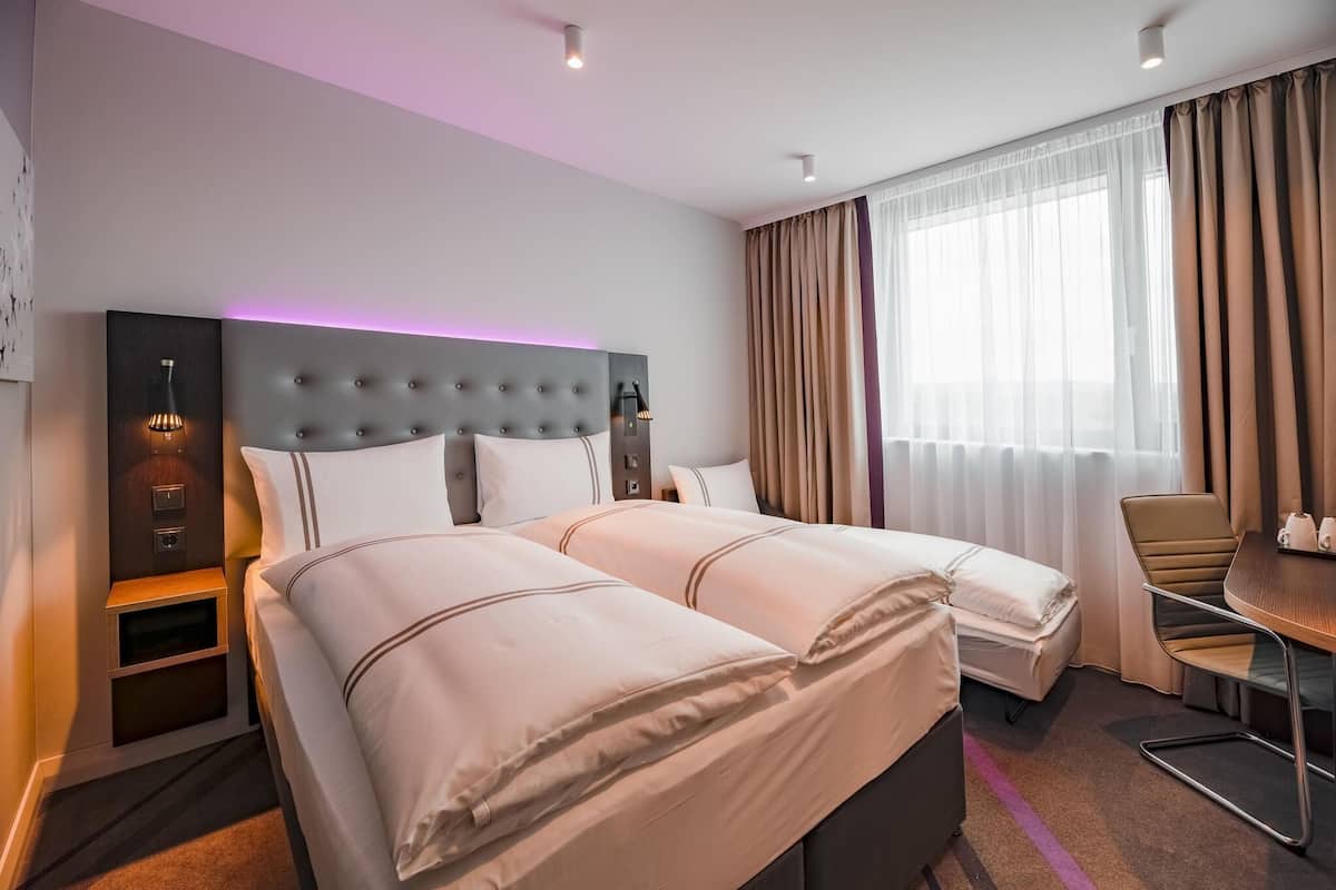 A hotel room with two beds, a desk, a chair, a lamp, and a window with curtains.