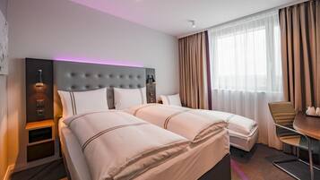 A hotel room with two beds, a desk, a chair, a lamp, and a window with curtains.