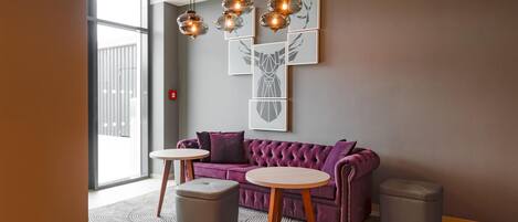 Una habitación moderna con un sofá morado, dos mesas redondas y una obra de arte geométrica en la pared.