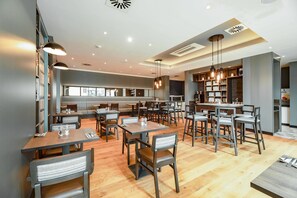 A modern restaurant with multiple dining tables and chairs, a bar area, and a kitchen visible in the background.