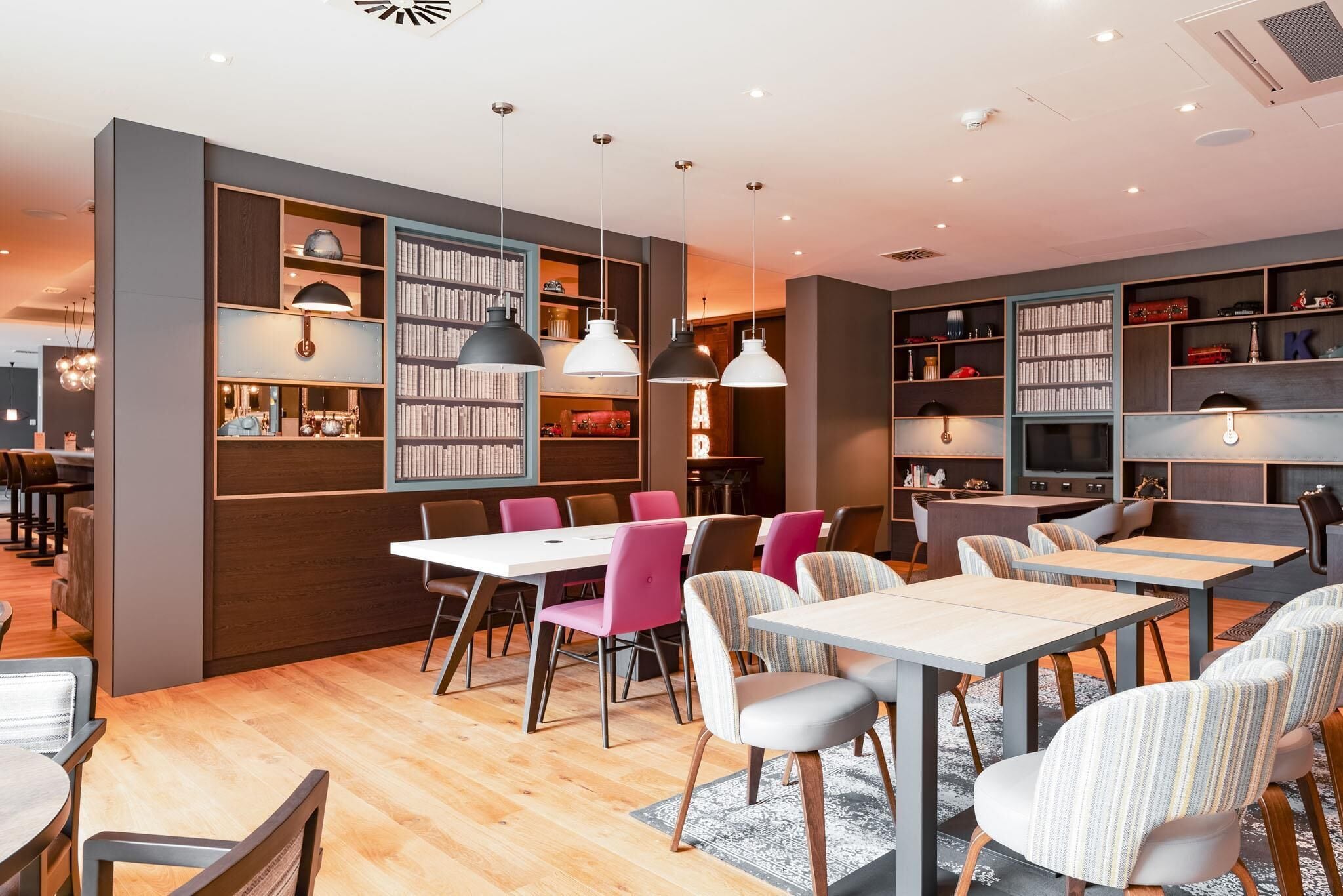 A modern dining area with tables and chairs, a bookshelf, and pendant lighting.