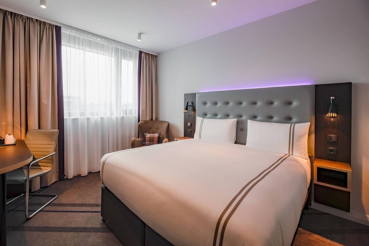 A hotel room with a large bed, a desk, a chair, and a window with curtains.
