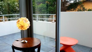 Ein Balkon mit Tisch, Stuhl und einer dekorativen Lampe, mit Blick auf Grün hinter Glas.