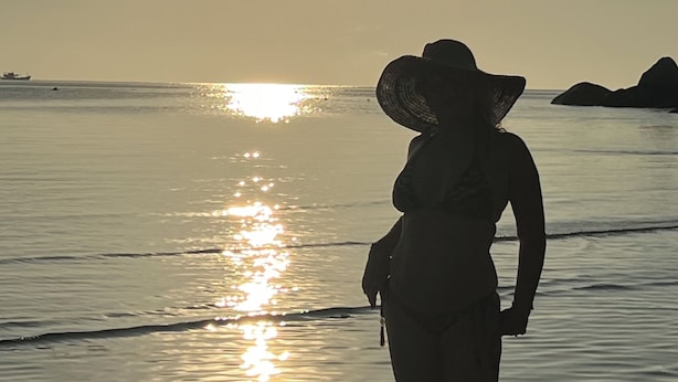 Eine Silhouette einer Person, die am Strand steht, während die Sonne am Horizont sinkt.
