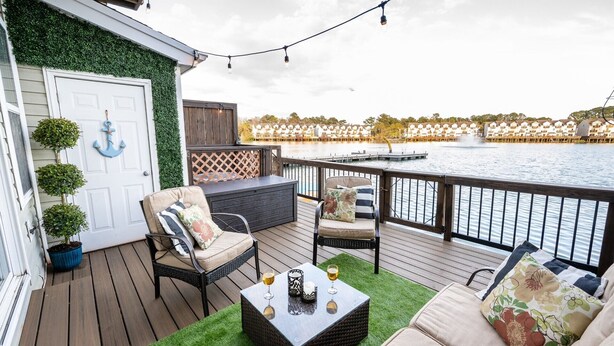 Eine Terrasse mit Gartenmöbeln, einem kleinen Tisch und Blick auf ein Gewässer.