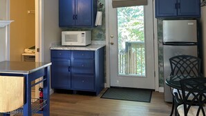 A compact kitchen with blue cabinets, a microwave, a refrigerator, and a dining area with a chair. - Beautiful sunset on John’s Pond (Mashpee)