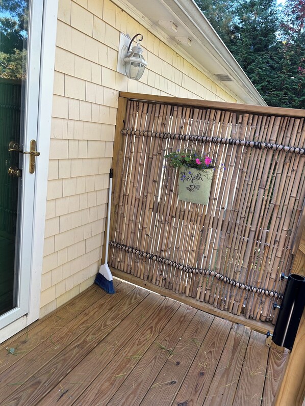 A wooden deck with a bamboo fence, a broom, and a potted plant with flowers.