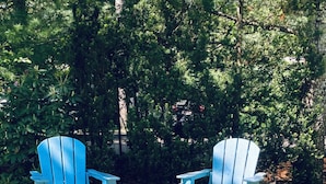 Two blue Adirondack chairs and a metal fire pit in a garden setting. - Beautiful sunset on John’s Pond (Mashpee)