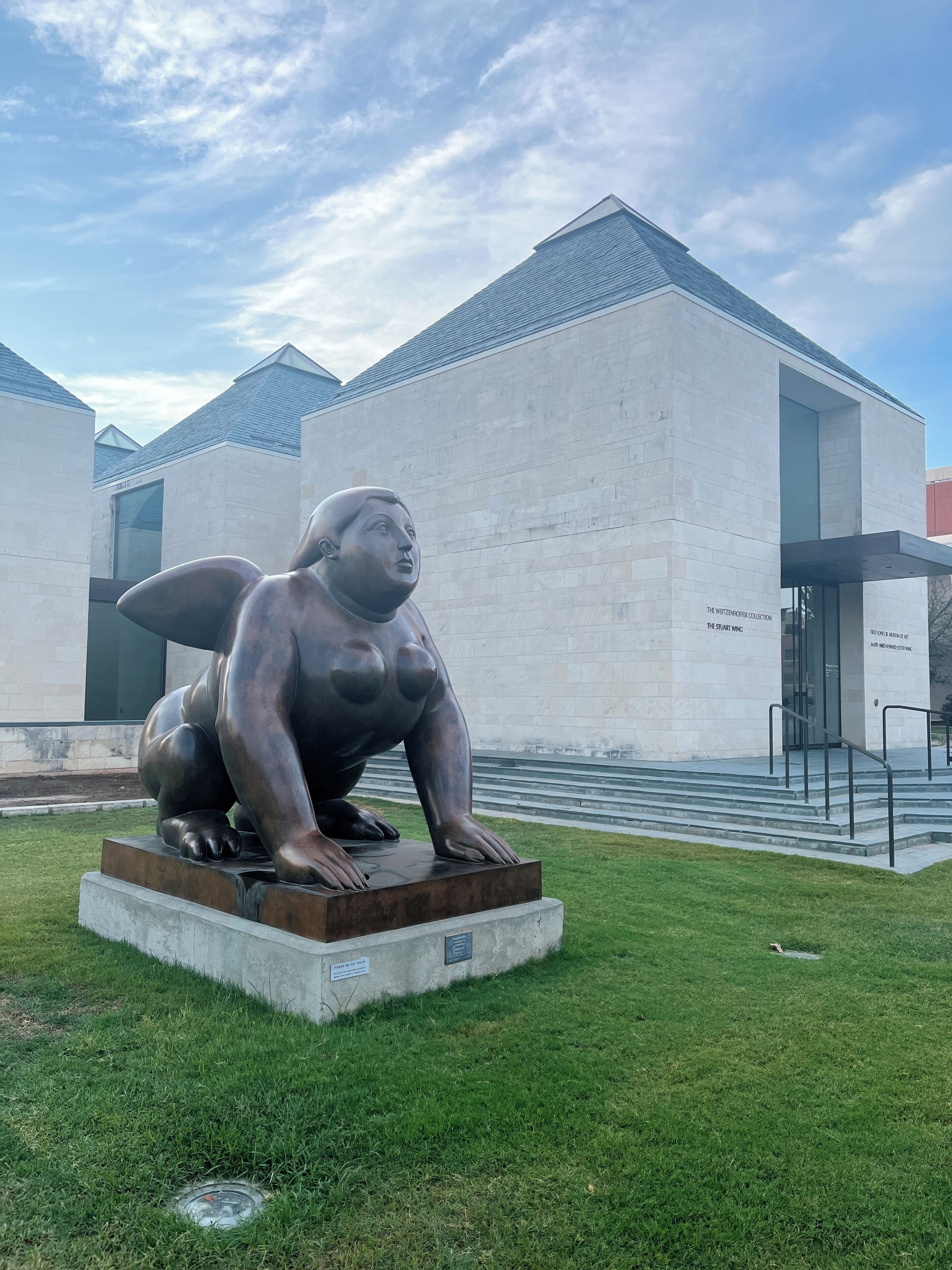 A sculpture of a seated figure in a public space with a building in the background.