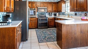 A kitchen with wooden cabinets, stainless steel appliances, and a patterned backsplash. - Game Room + Colorful Comfort (Norman)