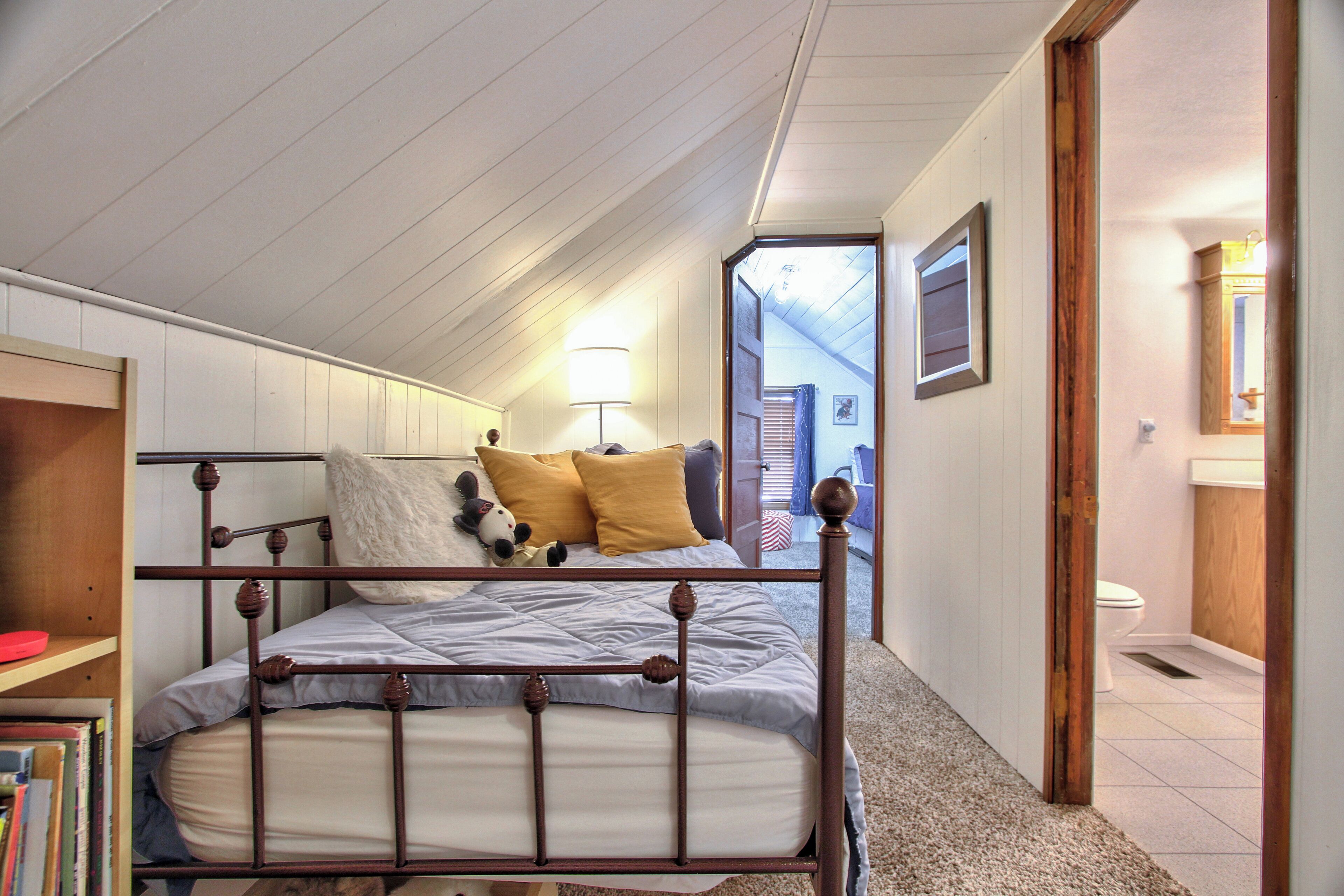 A bedroom with a metal bed frame, a bedside table, a lamp, and a view of the bathroom through an open door.
