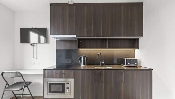 A modern kitchen with dark wood cabinets, a stainless steel microwave, a kettle, and a toaster.