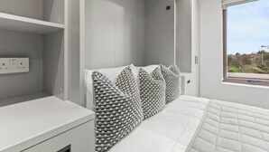 A modern bedroom with a bed, white walls, and a window with a view.
