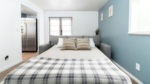 Een slaapkamer met een bed, een grijze bank, een plafondventilator en een raam.