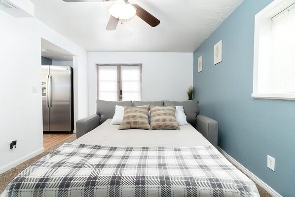 A bedroom with a bed, a grey sofa, a ceiling fan, and a window.