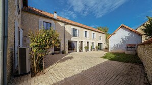 A courtyard with stone buildings, a paved walkway, and a small tree. - La Longère de Neuville (Neuville-de-Poitou)