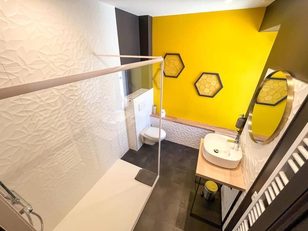 A modern bathroom with a yellow accent wall, a white toilet, a sink with a mirror, and a shower area.