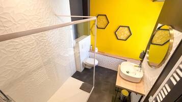 A modern bathroom with a yellow accent wall, a white toilet, a sink with a mirror, and a shower area.