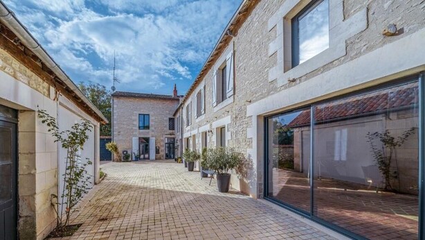 A courtyard with a paved walkway, stone buildings, and potted plants. - La Longère de Neuville (Neuville-de-Poitou)