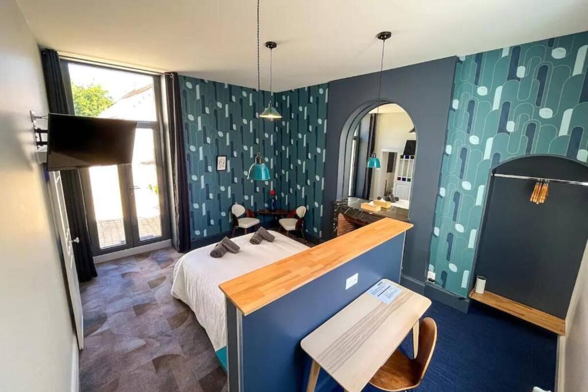 A hotel room with a bed, a desk, a chair, a mirror, and a wardrobe.