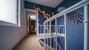 A hallway with a blue wall, white railing, and a wooden bookshelf. - La Longère de Neuville (Neuville-de-Poitou)