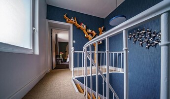 Corredor com parede azul, guarda-corpo branco e estante de madeira.