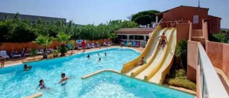 A swimming pool with a slide, surrounded by lounge chairs and a building.