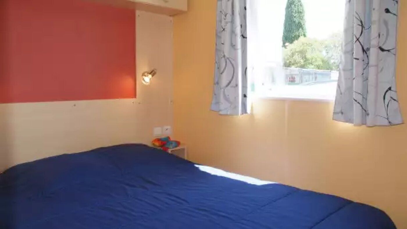 Ein Schlafzimmer mit einem Bett, einem Nachttisch, einer Lampe und einem Fenster mit Vorhängen.