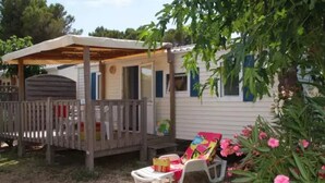 A mobile home with a covered porch, a fenced yard, and a garden with pink flowers.