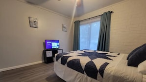 Ein Schlafzimmer mit Bett, Fernseher auf einem Schrank, einem Fenster mit Vorhängen und einer Ziegelwand.