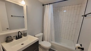 Ein Badezimmer mit Waschbecken, Toilette, Duschkabine und einem Spiegel mit Beleuchtung darüber.