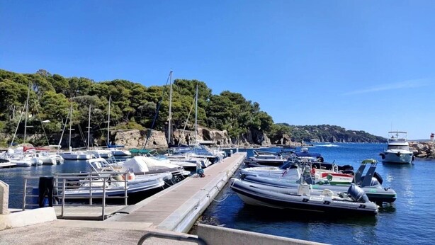 Ein Yachthafen mit Booten, die an einer hölzernen Pier vertäut sind, umgeben von felsigen Klippen und dichtem Grün.